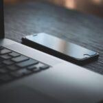 iPhone placed beside a laptop computer on a desk, representing mobile technology and digital connectivity.